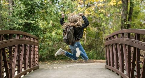 Girl on bridge with backpack jumping in celebration